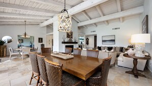 A spacious dining area with a wooden table and wicker chairs, a chandelier, and a fireplace in the background. - LQ001 - 3 bedroom 3 bath with pool (La Quinta)