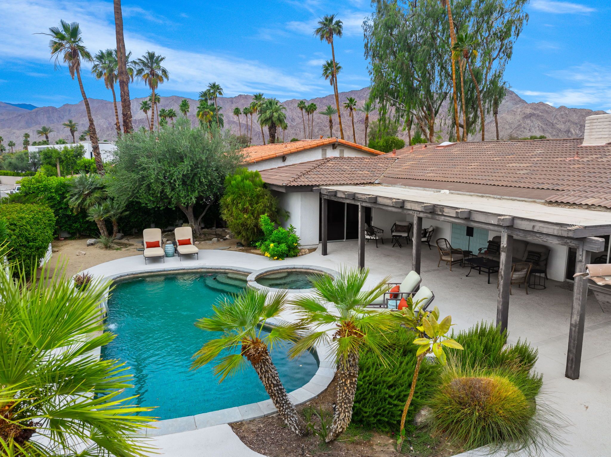A pool area with lounge chairs, a covered patio, and a mountainous backdrop.