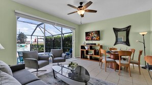 A spacious living area with a glass door leading to a balcony, a ceiling fan, and a dining setup with chairs and a table. - Windsor Hills 3 Bedroom Private Pool Townhome (Kissimmee)