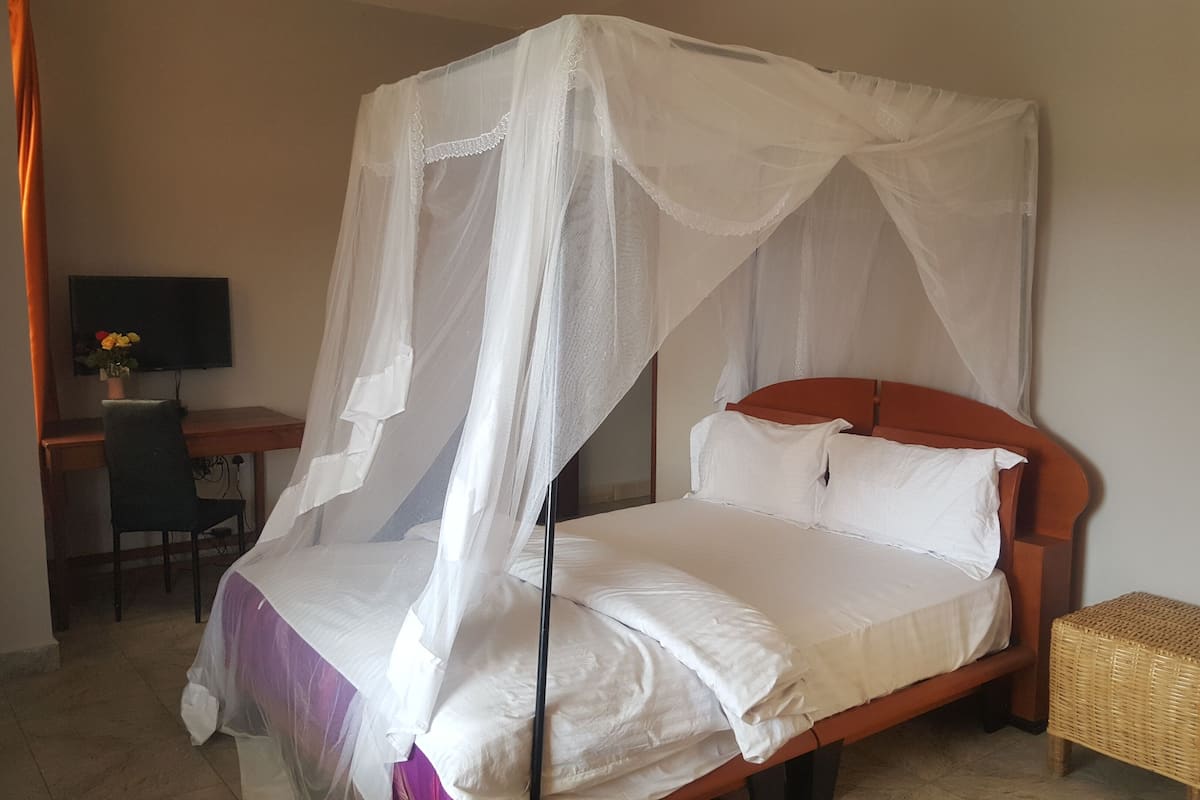A single bed with a wooden headboard, a white canopy, and a small wicker stool beside it.