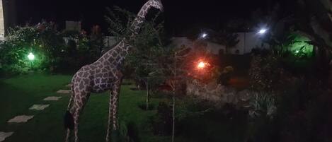 A giraffe statue in a garden with stone pathways and green plants.