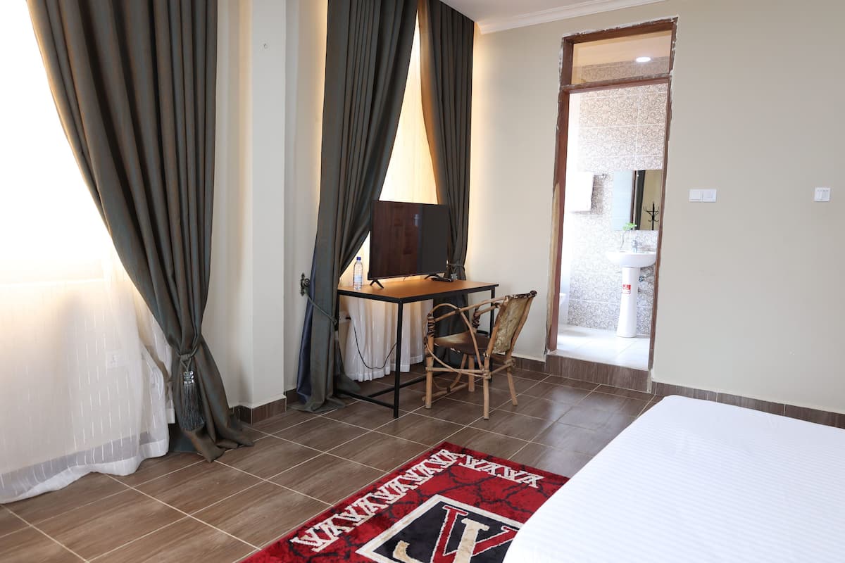 A hotel room with a bed, a desk, a chair, and a bathroom visible through an open door.