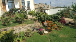 A well-maintained garden with various plants and flowers, a stone wall, and a house with large windows and a tiled roof. - Guest House in Arusha -Nanofilter Family (Arusha)