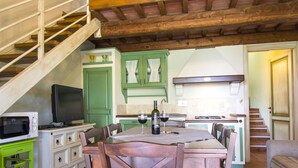 A dining area with a table set for two, a television, and a kitchen in the background.