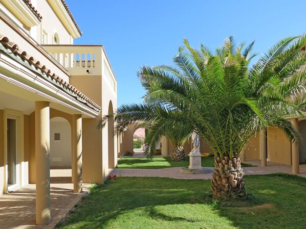 Un patio con una palmera, una estatua y un edificio con arcos y columnas.