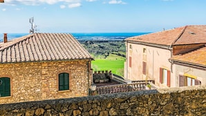 A stone building with a tiled roof overlooking a green landscape and a body of water.