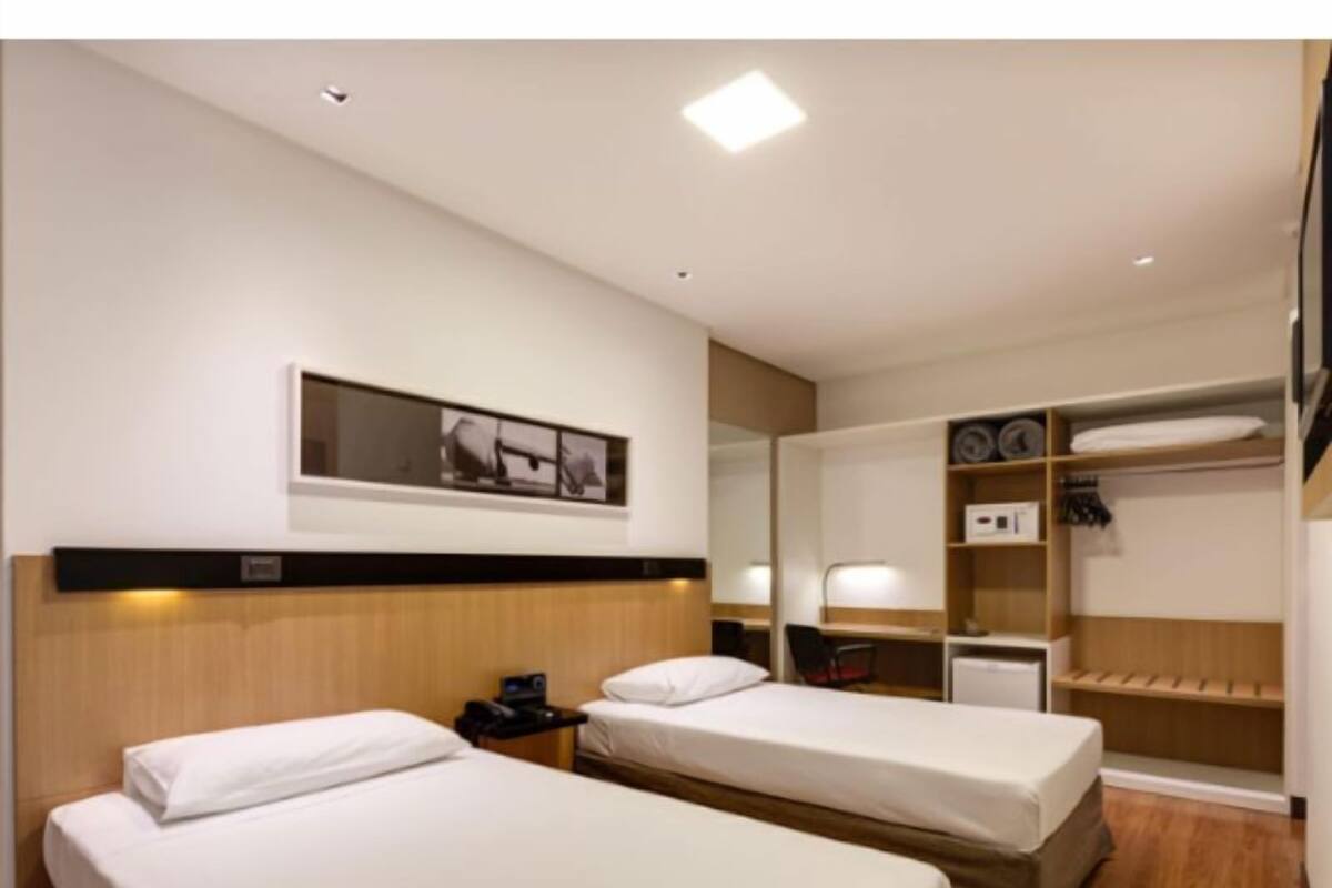 Une chambre d’hôtel avec deux lits simples, un bureau avec une chaise, un miroir et une armoire avec des étagères.