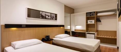 Ein Hotelzimmer mit zwei Einzelbetten, einem Schreibtisch mit Stuhl, einem Spiegel und einem Kleiderschrank mit Regalen.