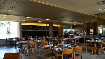 Un restaurante espacioso con varias mesas y sillas, una zona de bar y amplios ventanales que permiten la entrada de luz natural.