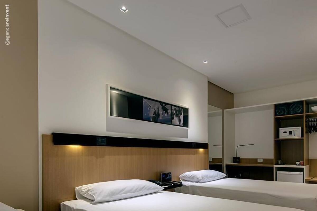 Une chambre d’hôtel avec deux lits simples, un téléviseur à écran plat fixé au mur, un petit bureau avec une chaise et une armoire avec un miroir.