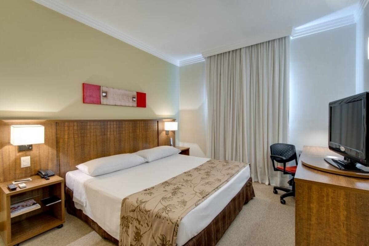 Une chambre d’hôtel avec un grand lit, des lampes de chevet, un bureau avec un ordinateur et une télévision.