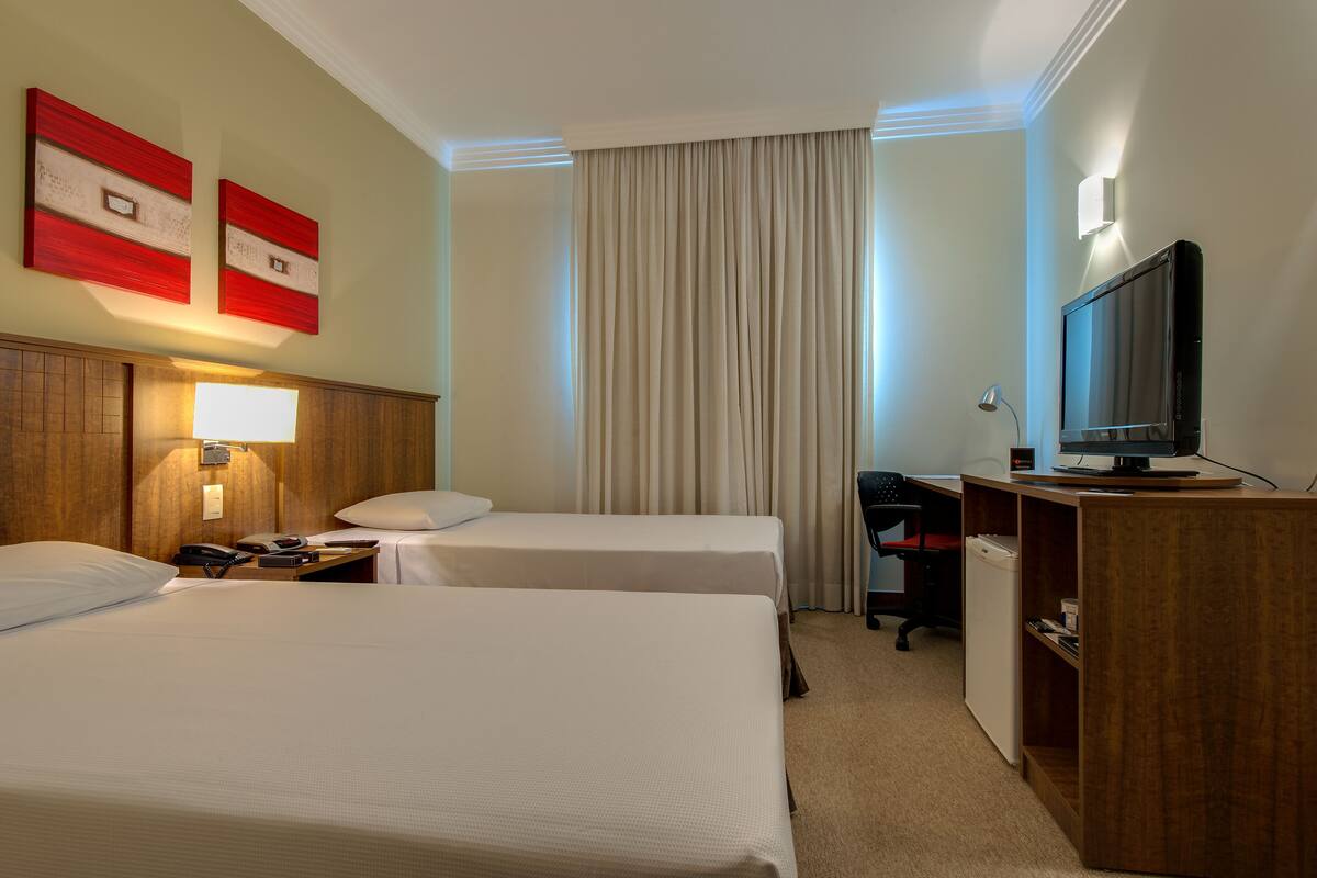 Une chambre d’hôtel avec deux lits, un bureau avec un ordinateur, une télévision et un minibar.