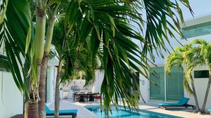 Ein Swimmingpool mit Liegestühlen, Essbereich und Palmen.