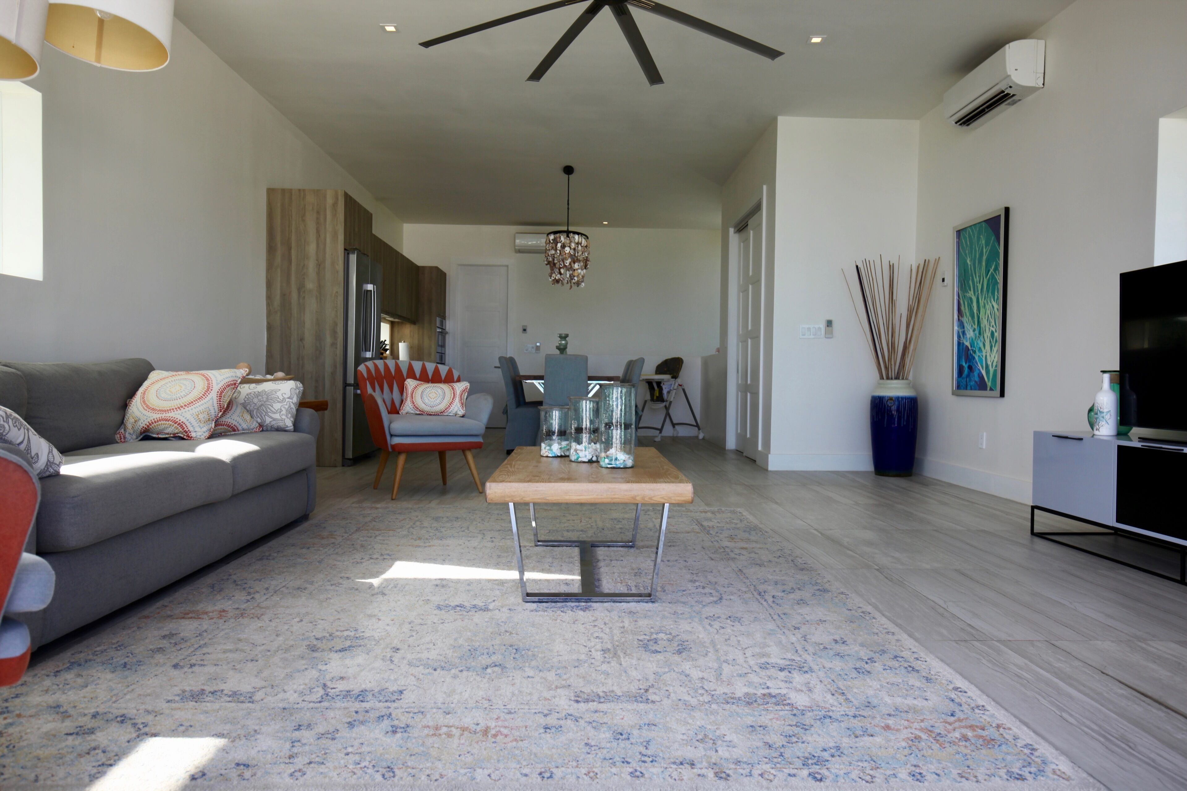 Una sala de estar moderna con un sofá gris, una mesa de centro de madera y un comedor con sillas y una araña.