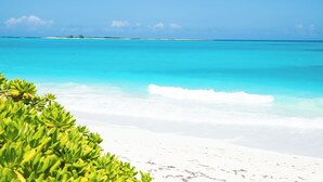 Ein Strand mit klarem türkisblauem Wasser, weißem Sand und grüner Vegetation.