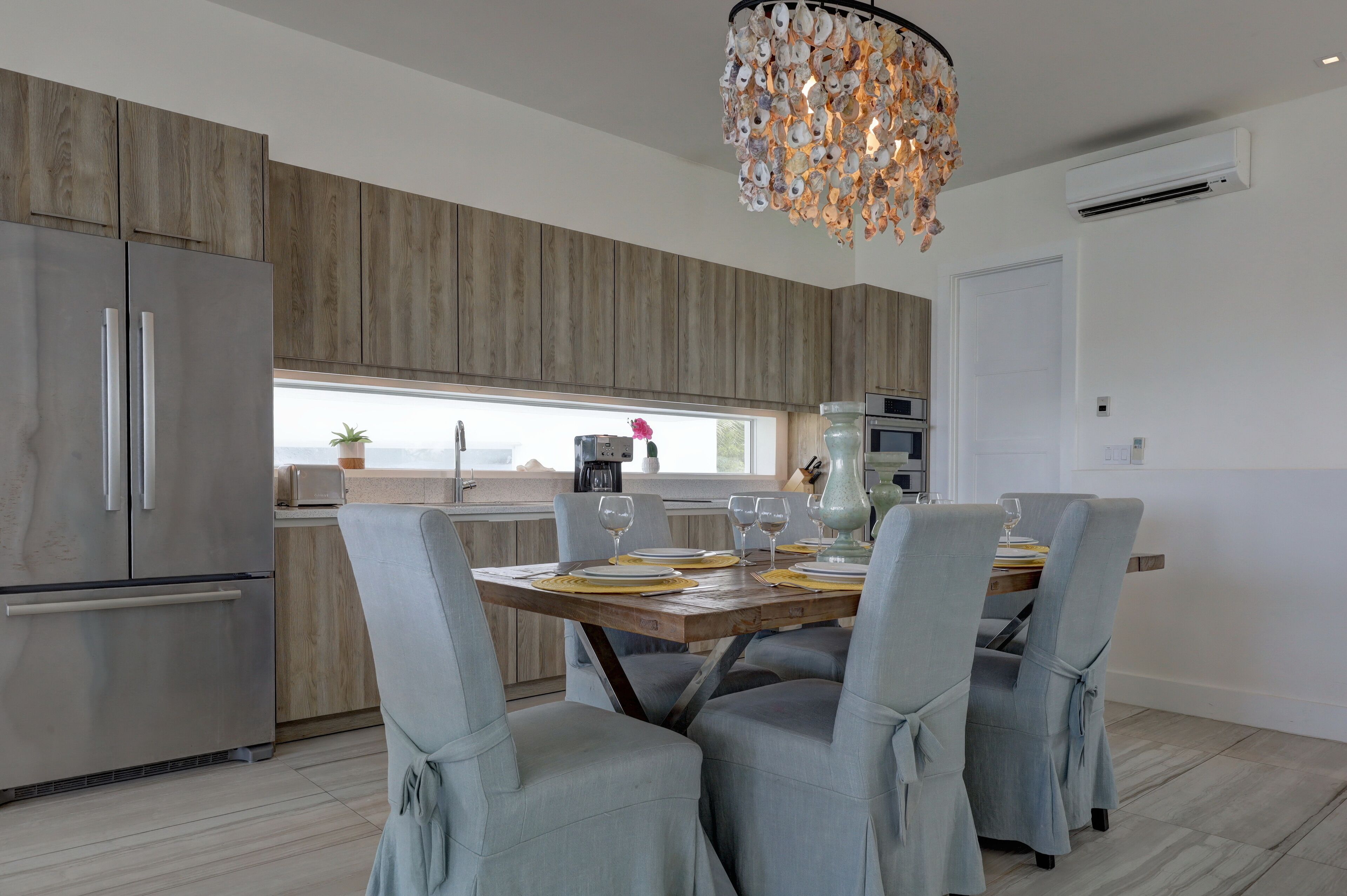 A modern kitchen with wooden cabinets, a stainless steel refrigerator, and a dining table set for four.
