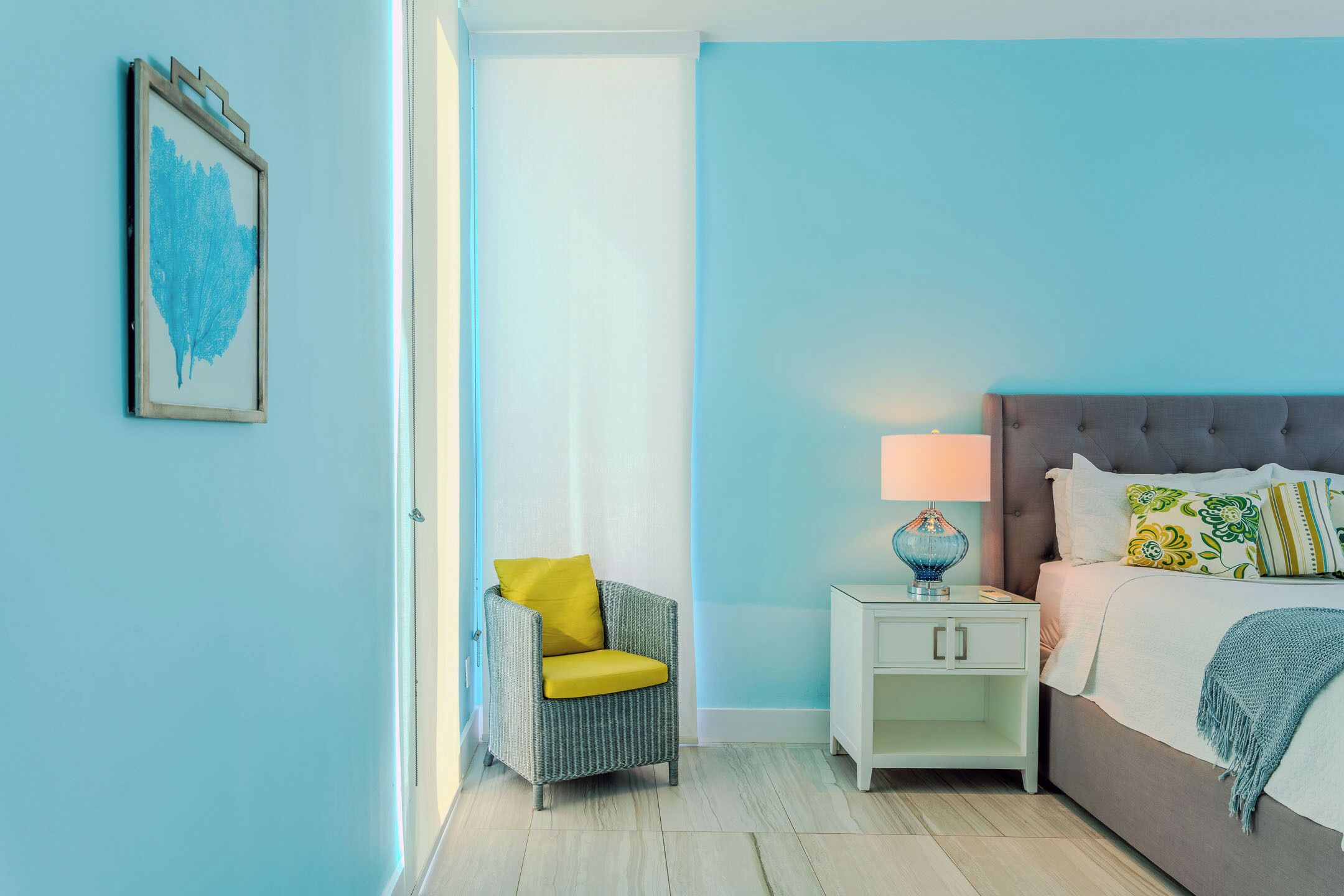 A bedroom with a bed, nightstand, chair, and a framed picture on the wall.