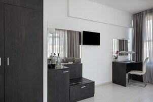 Ένα σύγχρονο υπνοδωμάτιο με μια σκούρα ξύλινη ντουλάπα, ένα γραφείο με καρέκλα, μια τηλεόραση επίπεδης οθόνης και έναν μεγάλο καθρέφτη.