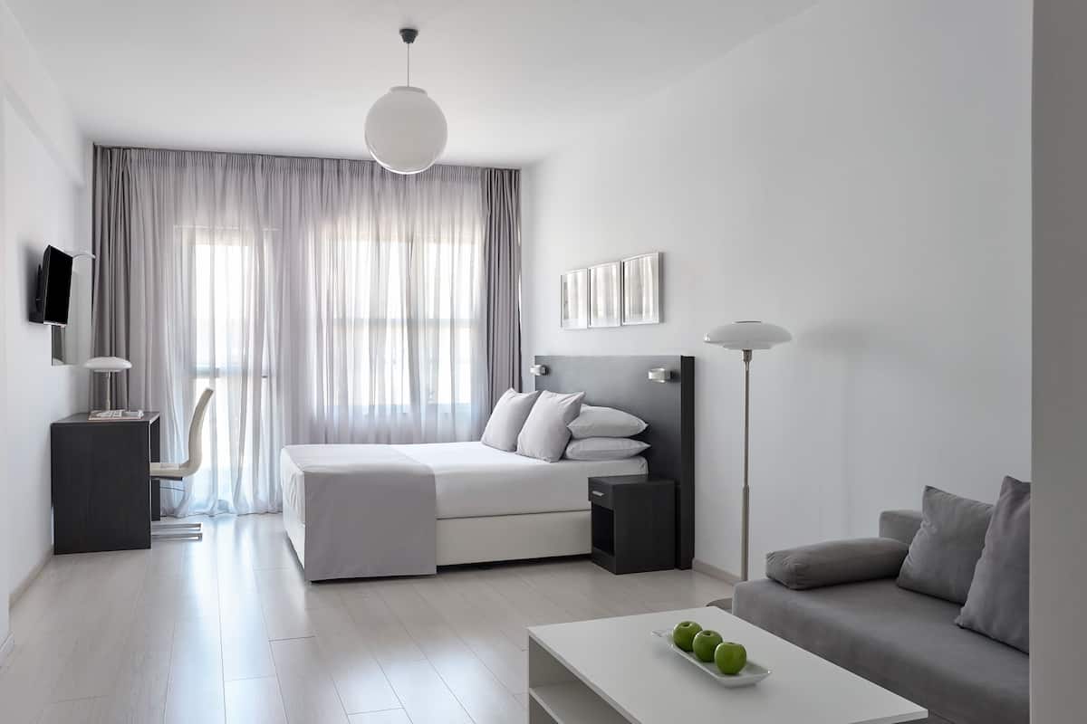 A modern hotel room with a bed, bedside table, lamp, and a sofa.
