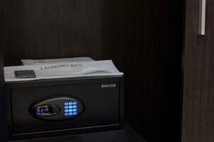 Ένα μαύρο ηλεκτρονικό χρηματοκιβώτιο Secustar με ψηφιακό πληκτρολόγιο και μια τσάντα για τα ρούχα τοποθετημένη στην κορυφή.