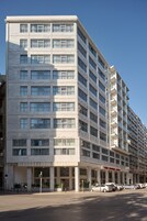 Ένα πολυώροφο ξενοδοχείο με μια μοντέρνα πρόσοψη, μεγάλα παράθυρα και έναν χώρο στάθμευσης με αρκετά αυτοκίνητα.