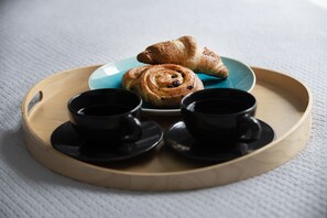 Sininen lautanen, jonka päällä on kaksi croissantia ja kanelipullaa, sekä kaksi mustaa kuppia aluslautasilla.