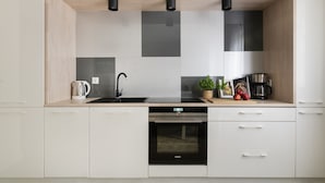 Une cuisine moderne avec des meubles blancs, un lave-vaisselle noir et une machine à café.