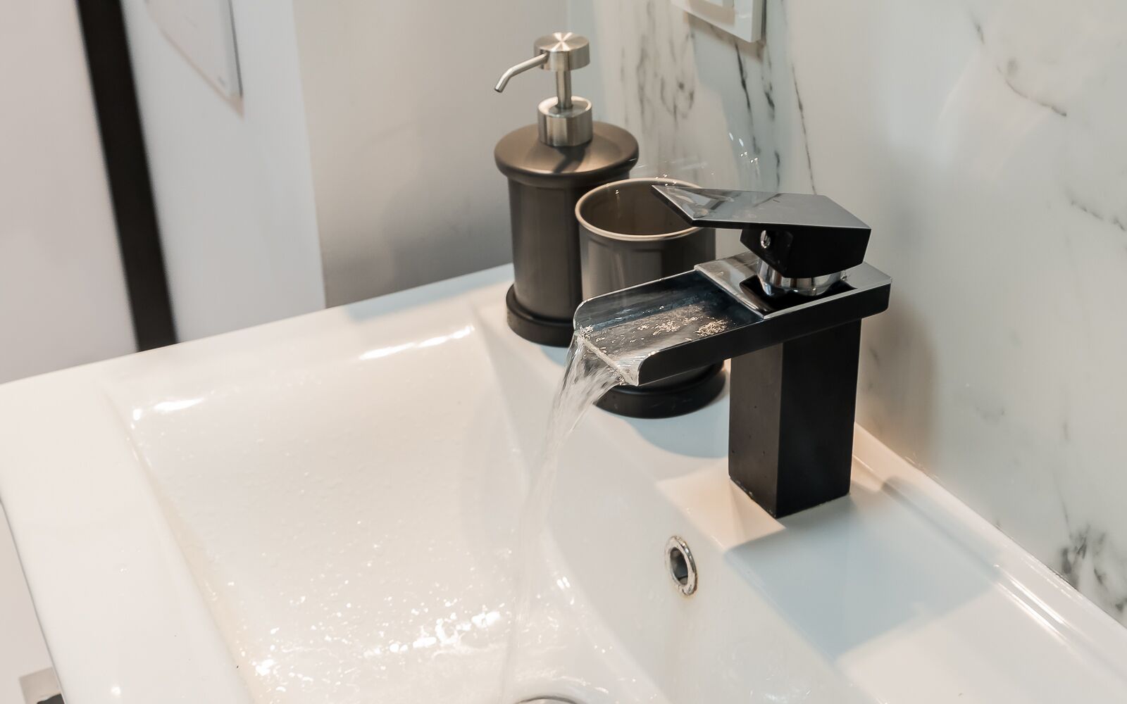A modern bathroom with a white sink, a black faucet, and a soap dispenser.