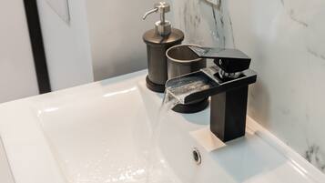 A modern bathroom with a white sink, a black faucet, and a soap dispenser.