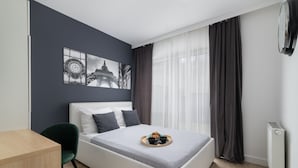 Une chambre moderne avec un lit, un bureau et une chaise. Il y a deux tableaux au mur, une fenêtre avec des rideaux et un radiateur.
