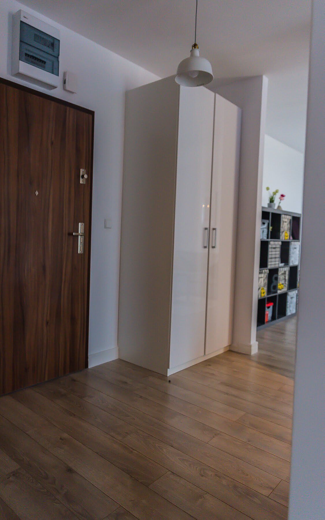 Una habitación con puerta de madera, un armario blanco y una lámpara colgante.