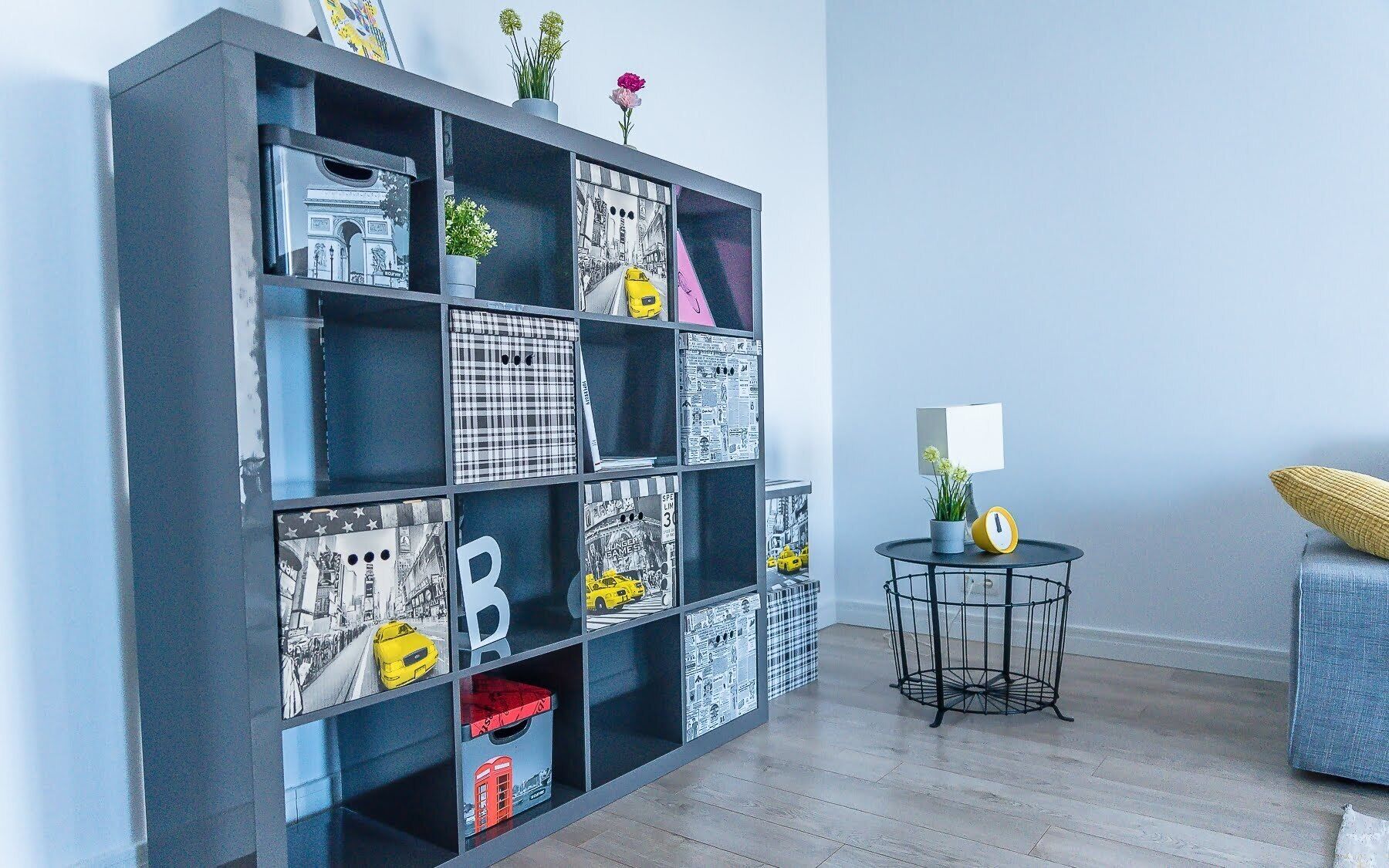 A modern living room with a dark blue bookshelf filled with various decorative items and a small round table with a lamp and a clock.