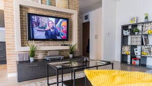 A modern living room with a flat-screen TV mounted on a brick wall, a dark entertainment unit, a glass coffee table, and a yellow sofa. - Easy Rent Apartments - SKY (Lublin)