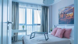 A modern bedroom with a bed, a desk, and a cityscape painting. - Easy Rent Apartments - SKY (Lublin)
