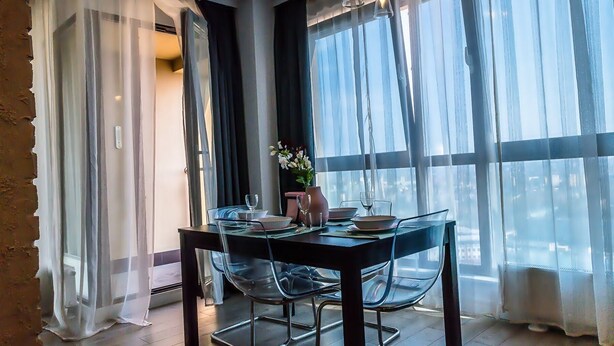 A dining area with a table set for two, a vase with flowers, and sheer curtains. - Easy Rent Apartments - SKY (Lublin)