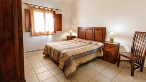 Un dormitorio con una cama de madera, dos mesitas de noche con lámparas, una silla de madera y una ventana con cortinas.