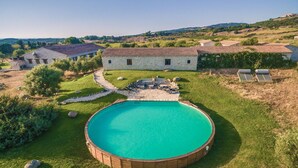 Una casa de piedra con piscina rodeada por una terraza de madera y un césped.
