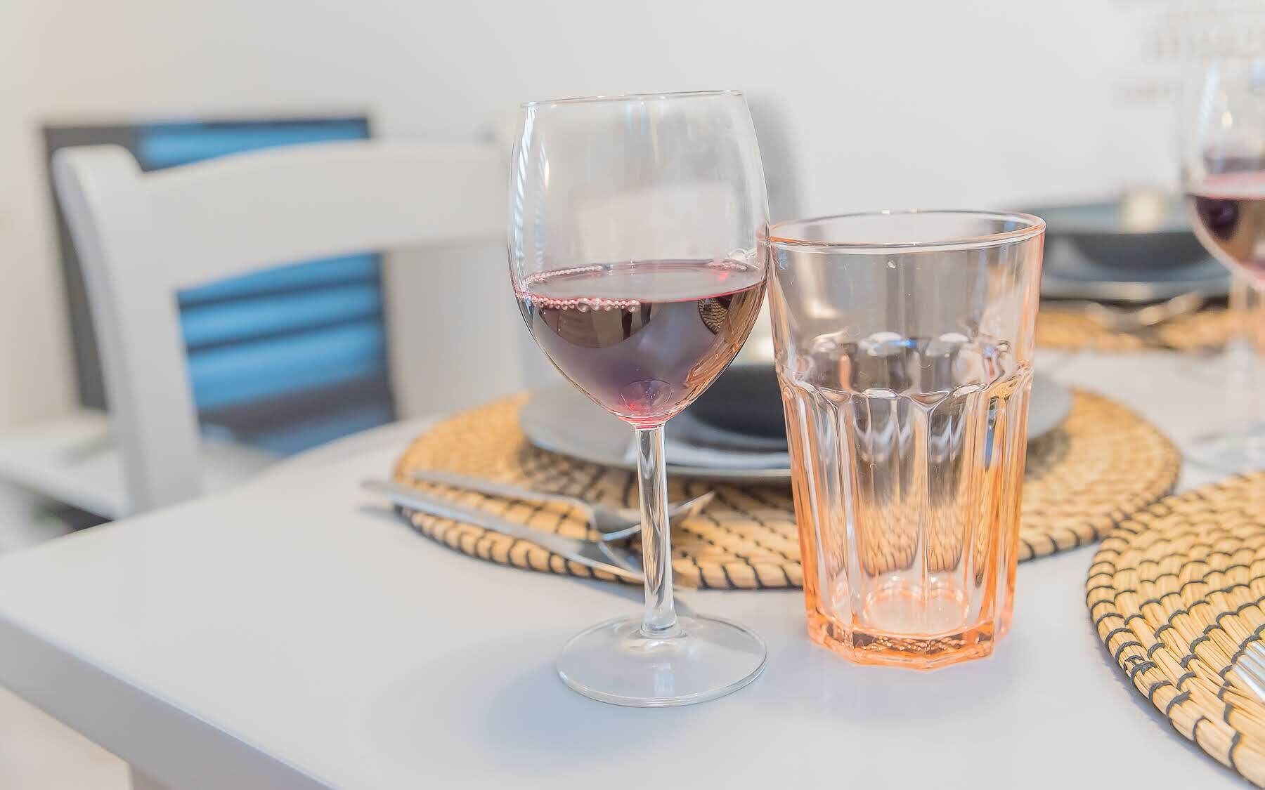 Dos copas de vino tinto sobre una mesa blanca con posavasos tejidos.