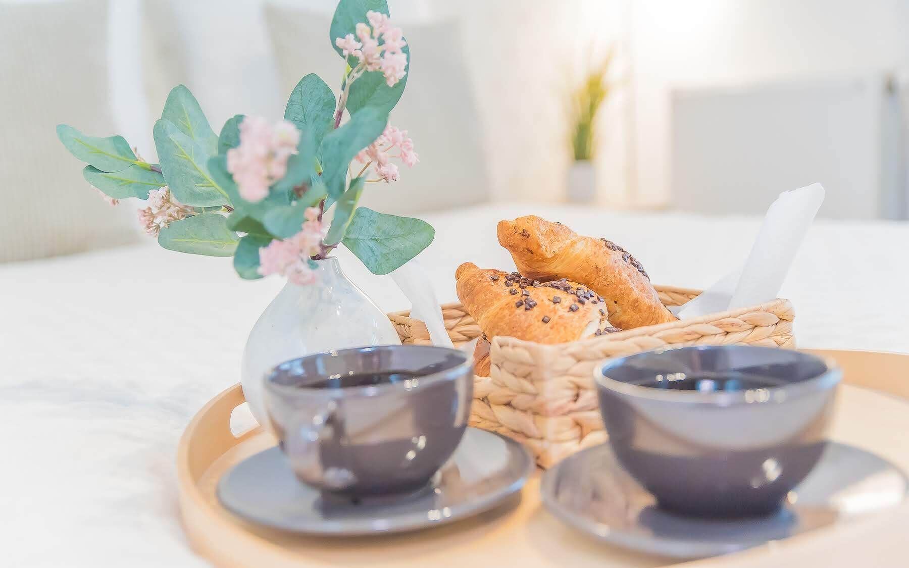 Una bandeja con dos tazas de café, un florero con flores y una cesta de pan.