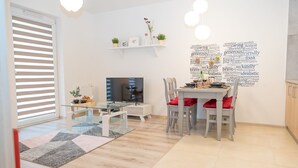 Una sala de estar moderna con una mesa de comedor de vidrio, sillas blancas, un televisor de pantalla plana y una obra de arte con una nube de palabras en la pared.