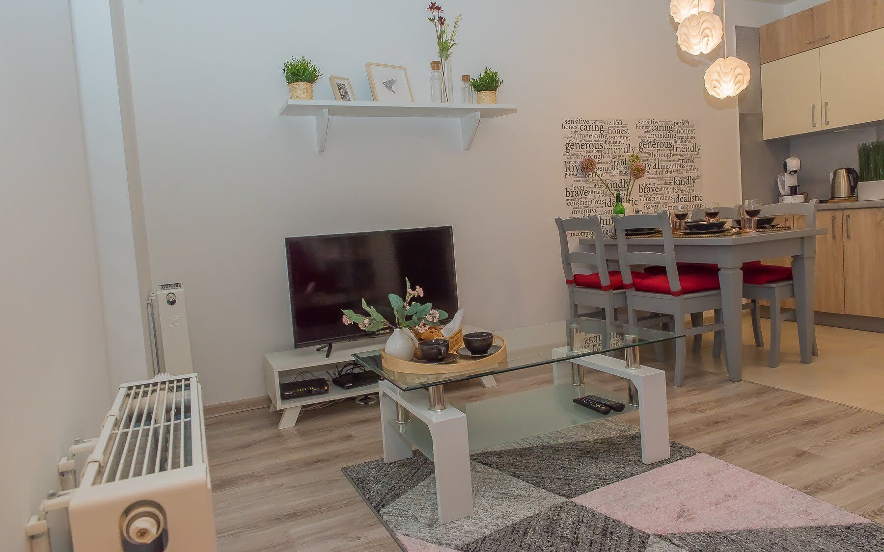 A modern living room with a flat-screen TV, a glass coffee table, and a dining area with red chairs.