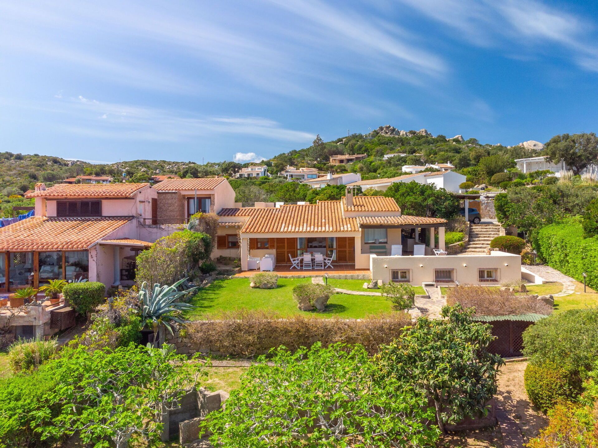 A hillside villa with multiple buildings, a well-maintained garden, and a view of the surrounding landscape.