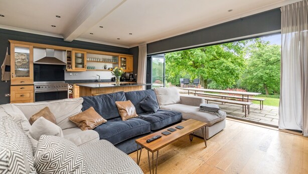 A modern living room with a sofa, coffee table, and a kitchen area with cabinets and a stove. - Poundgate Park Holiday House 8 Bedroom in 2 adjoining properties ,1h from London (Crowborough)