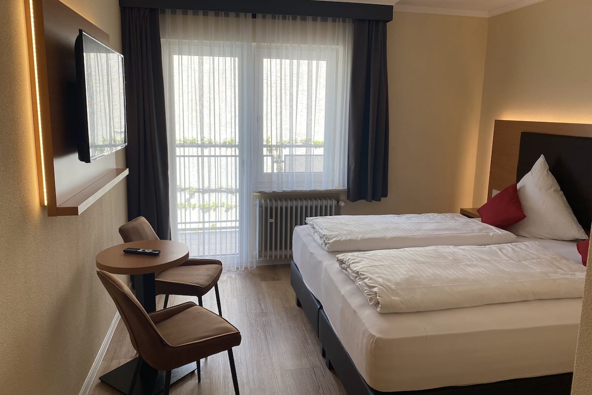 A hotel room with two beds, a desk, chairs, a TV, and a window with curtains.