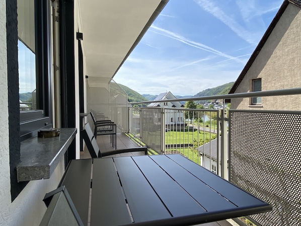 A balcony with a table and chairs, overlooking a green landscape and buildings.