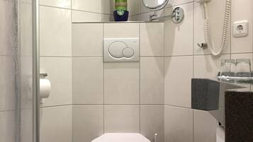 Casa de banho com sanita, bidé, porta-toalhas, espelho e chuveiro com porta de vidro.