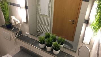 Ein modernes Badezimmer mit Dusche, Handtuchhalter, Toilette und Blumentöpfen auf der Ablagefläche.