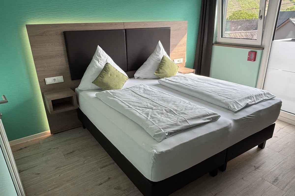 A neatly made bed with white linens and two pillows, a wooden headboard, and a small bedside table with a lamp.