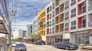 A multi-story building with balconies, a variety of shops on the ground floor, and parked cars along the street. - TJ PATONG HOTEL - Prime Location by OTOP Market & Sea (Patong)
