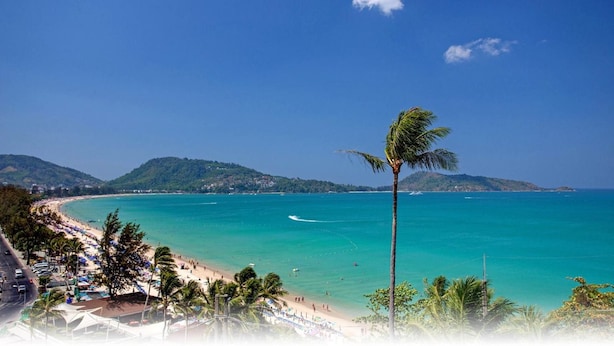 A beach with clear turquoise water, a palm tree, and a hilly landscape in the background. - TJ PATONG HOTEL - Prime Location by OTOP Market & Sea (Patong)